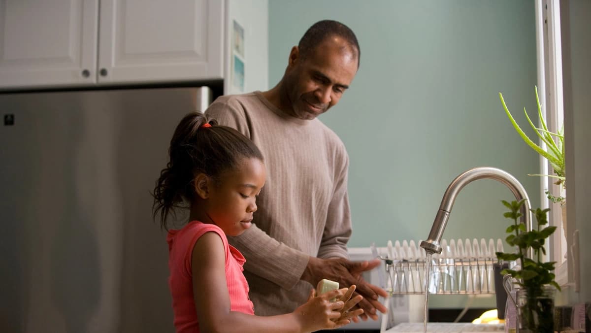 daughter washing hands while father talks to her