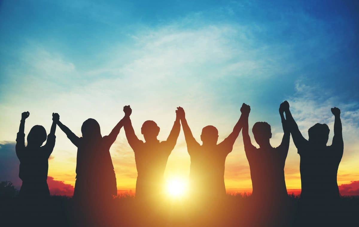 group of friends with their clasped hands raised at sunset