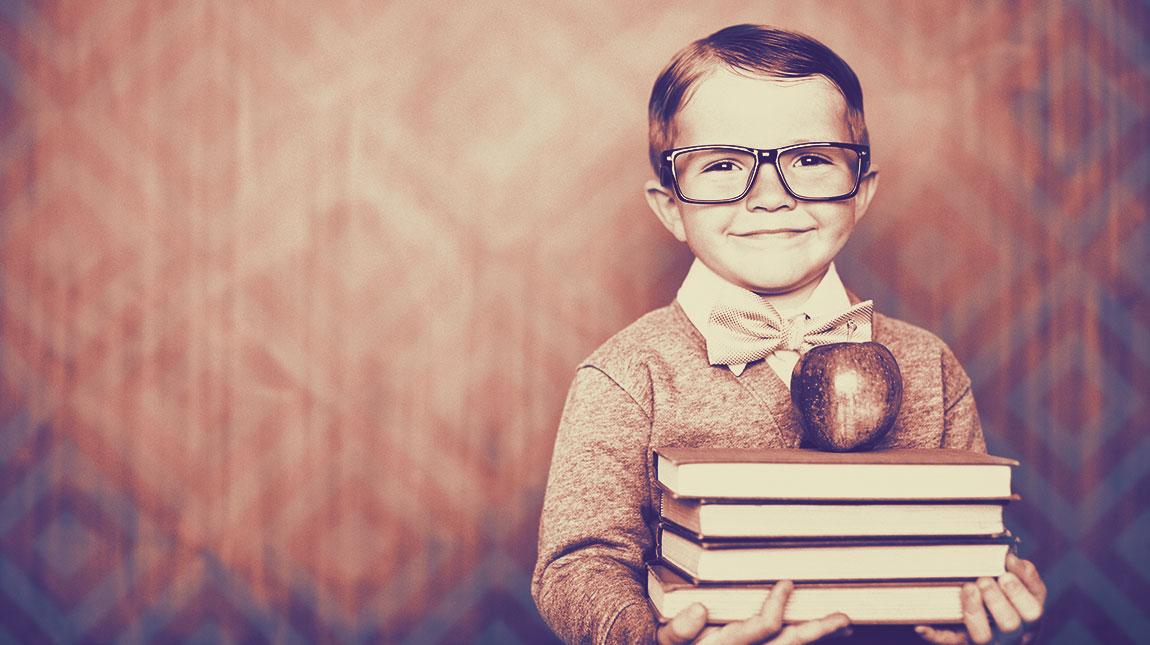 little boy with glasses holding a stack of books with an apple on top