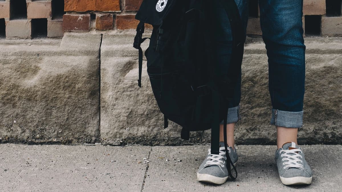 feet person standing holding backpack against brick wall