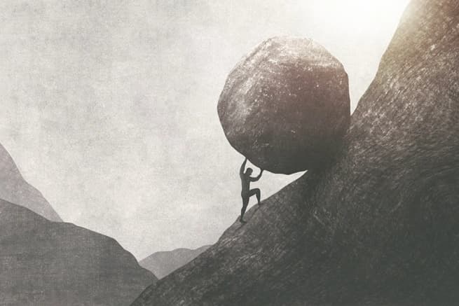 man lifting large boulder up hill